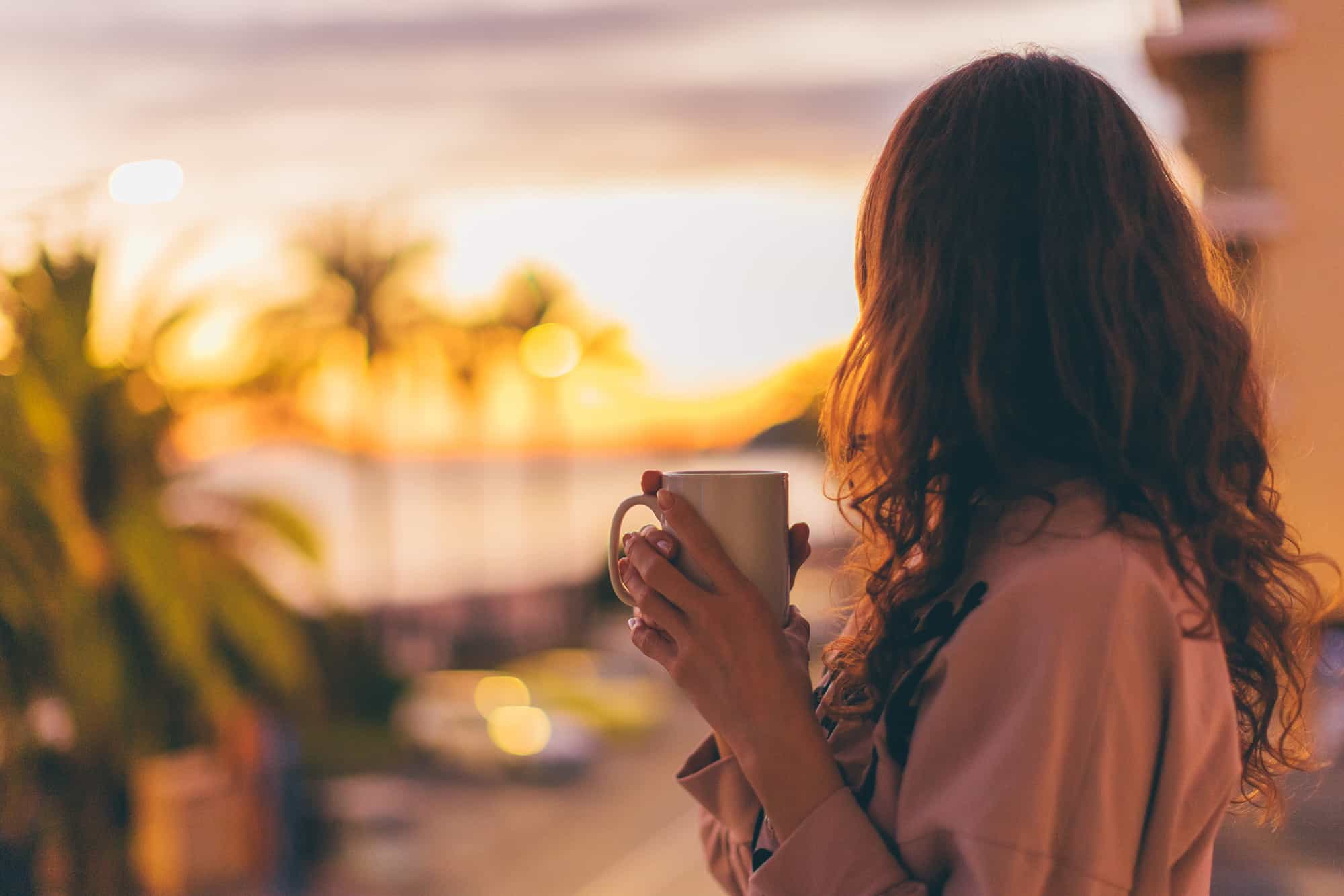 Lonely romantic girl drinking coffee looking at sunset.